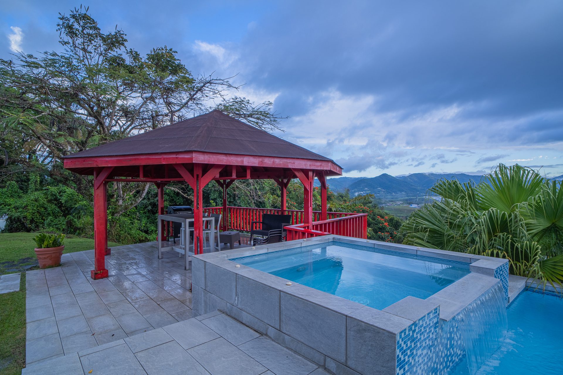The raised spa and red timber pavilion beside the pool, framed by palms and a broad mountain view
