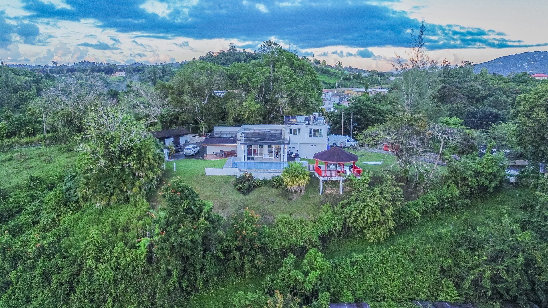 Aerial view of Hacienda La Promesa nestled among dense green hills, with the pool and red pavilion visible below