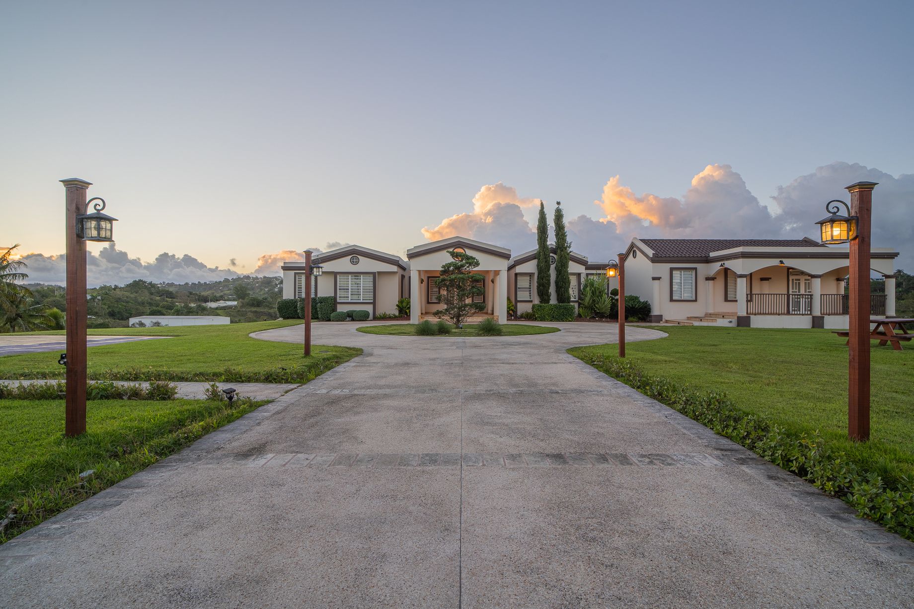 Long entrance drive between open lawns leading toward both homes beneath gold-edged evening clouds