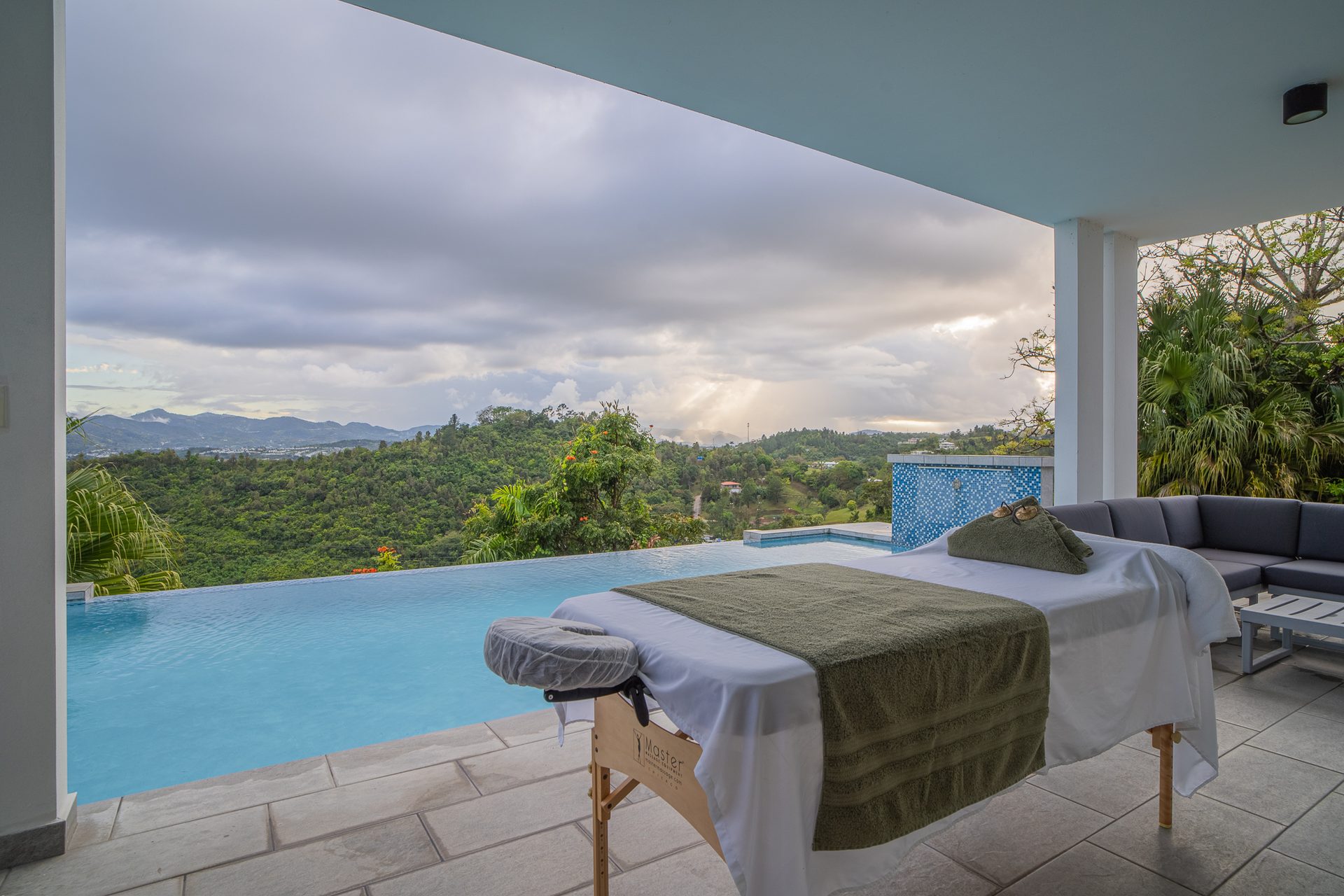 A massage table prepared beneath the covered pool terrace, facing the infinity edge and the mountains beyond